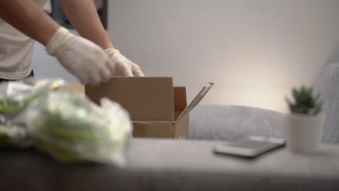 Asian male unpacking take away Food box, grocery online purchase delivery service during corona virus covid19, on the gray couch at home, unpack carton parcel package, vegetable food supply shipping, 