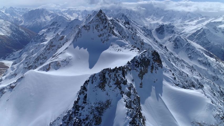 Helicopter flight over incredible epic mountain landscape winter snow covered sharp peaks of many rocky volcanic slopes. Mountains tops. Fairy nature Scandinavia Himalayas Tibet. Cumulus clouds sunny. | Shutterstock HD Video #1051598923