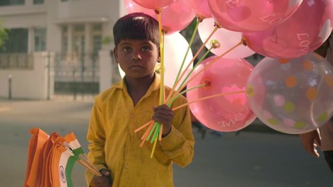 A poor, unprivileged male kid on a street selling balloons and Indian national tricolour flag on the road during the republic, a national day. 