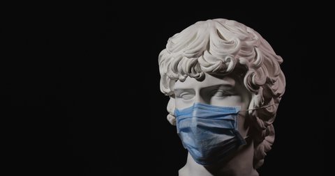 Epic studio close up shot of rotating gypsum head with dramatic light wearing medical face mask. Rotation of white antinous sculpt with face shield on it. On black background isolated 4k