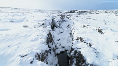 Aerial drone shot flying above frozen Icelandic landscape covered with white snow. Top view from sky over river, valley, rocks, stones and trees. Winter holidays in Thingvellir national park, Iceland
