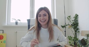 Smiling young woman working at home. Girl speaking looking at camera talking making video chat or conference call. Happy female holding tablet computer, 4k webcam view slow motion