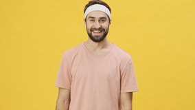 A happy young athletic man in sportswear is laughing to the camera isolated over a yellow background in studio