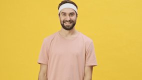 A handsome young athletic man in sportswear is laughing to the camera isolated over a yellow background in studio