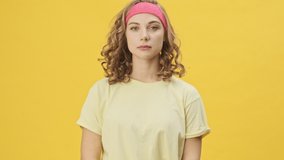 A beautiful young athletic woman in sportswear is smiling isolated over a yellow background in studio