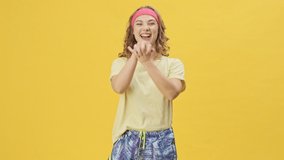 A pleased young athletic woman in sportswear is doing sport exercises moving her hands isolated over a yellow background in studio