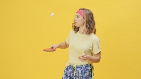 A happy smiling young athletic woman in sportswear is playing ping-pong isolated over a yellow background in studio