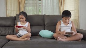 Asian sister and brother surfing the net or playing online games on smartphone at home. Modern communication and gadget addiction concept.
