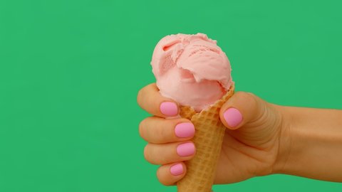 Time lapse of a female hand holding melting ice cream cone on green background, 4K