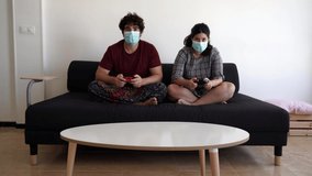 Video of a new normal situation after the 2020 coronavirus covid 19 sanitary crisis, the girl of a spanish couple wons a videogame match on a black couch wearing both their surgical masks