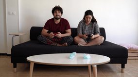 Video of a new normal situation after the 2020 coronavirus covid 19 sanitary crisis, the man of a spanish couple wons a videogame match on a black couch with two sanitary masks on the table