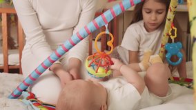 Toddler plays with his sisters. The concept of development of babies and care. 4K UHD still video camera, 2x slow motion.