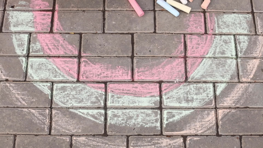 A child draws a rainbow on the asphalt. A little girl draws chalk in the park.
