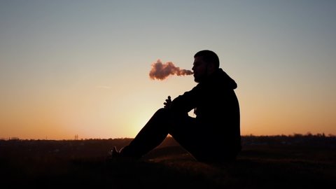 Steam from the vape. Silhouette of smoke at sunset. A man hovers with the help of vape. Beautiful smoke at sunset. Electronic cigarette and smoke. Healthy lifestyle. Refusal of cigarettes. Silhouette 