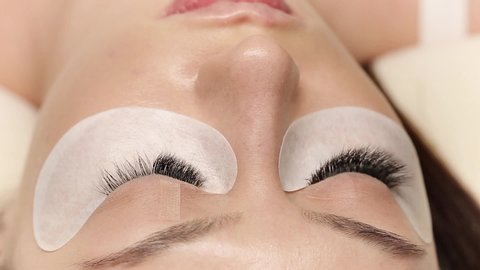 Eyelashes extensions. Fake eyelashes. Eyelash extension procedure.Close up portrait of woman eye with long eyelashes. Professional stylist lengthening female lashes. Master and client in beauty salon.