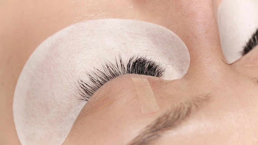 Eyelashes extensions. Fake eyelashes. Eyelash extension procedure.Close up portrait of woman eye with long eyelashes. Professional stylist lengthening female lashes. Master and client in beauty salon. | Shutterstock HD Video #1051650151