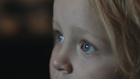 Slow motion close-up shot of a toddler girl being attracted with TV. Child blue eyes with screen reflection