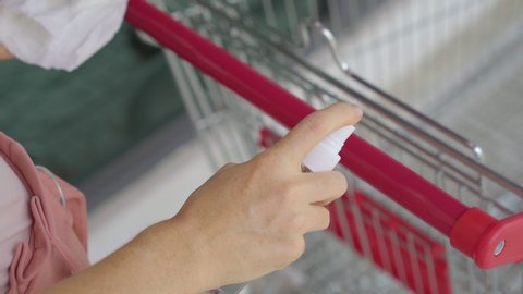 Young woman disinfecting a handle of a supermarket trolley in order to protect herself from contact with the infection. Social distancing concept. Covid protection concept.