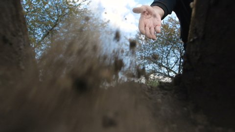 A hand of unrecognizable person in dark clothes throwing the first handful of earth into the grave against a blue sky with clouds. Point of view from the coffin on funeral.  Slow motion 200 fps
