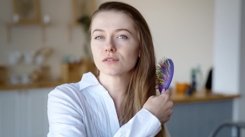Attractive cheerful woman dancing on bed and singing with comb like microphone at home