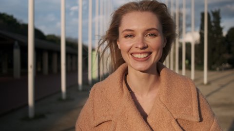 Portrait of cheerful blond girl happily looking in camera and showing tongue outdoor at sunset