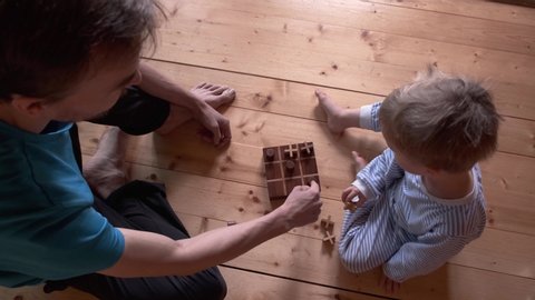 Child and father playing board game at home. Son and dad play rock paper scissors, then tic tac toe. Parent spend time with kid while quarantine and self-isolation. View from above.