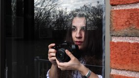 Caucausian female woman is using a DSLR camera lens to take pictures of the outside world thrrough a window while stuck at home
