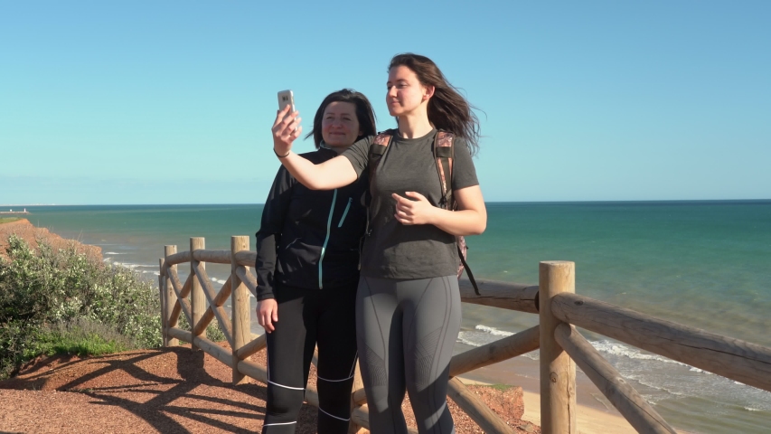 Successful, middle-aged woman with a young girl, on a cliff near the ocean, selfie by phone. Portugal. Vilamoura. Mother with daughter.