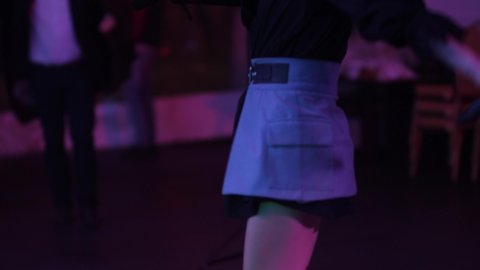beautiful bare legs of a young girl in a short skirt with high heels dancing to the music in a nightclub among the crowd