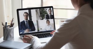 Over shoulder closeup view of business woman videoconferencing partners team by online video call virtual app. Remote worker conferencing colleagues group on pc laptop screen working from home office.