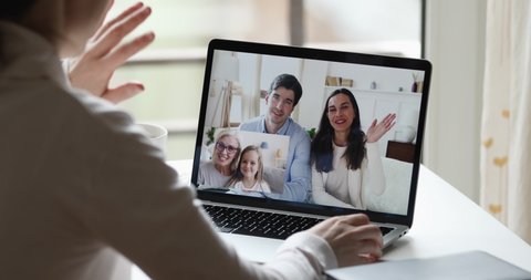 Young woman waving hand video calling long distance relatives by web cam. Happy big family chatting in conference group chat during social quarantine concept. Over shoulder closeup laptop screen view