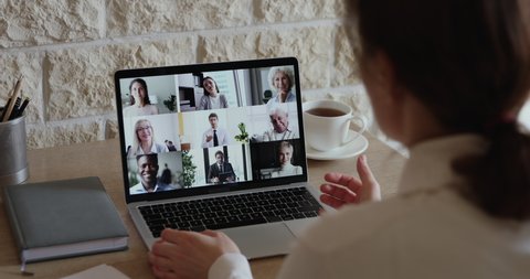 Over shoulder view of businesswoman video conferencing diverse business people team on laptop screen engaged in online group call, virtual corporate meeting using pc app for distance company teamwork.