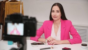 A female blogger online shoots a video about cosmetics. Shows and talks about lipstick. White room, camera on tripod.