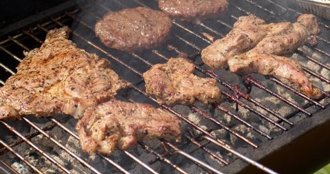 Tasty hamburger meat and pork grilling on smoking hot barbecue. Slow motion video. Outdoor food concept.