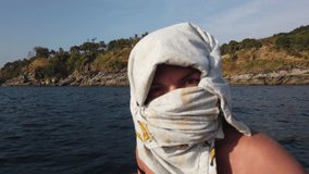 Girl in a boat that rushes along the shore covers her face with clothes from the sun
