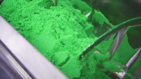 Colorful green chemical power being mixed inside an industrial ribbon mixer to produce chemical fertilizer. Shot in slow motion. Specialized industrial equipment, manufacturing machinery.