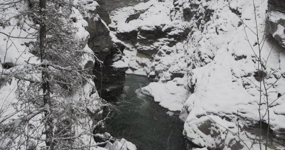 A small river flowing through the snow white mountains and landscape of Cascade Falls during winter - wide shot