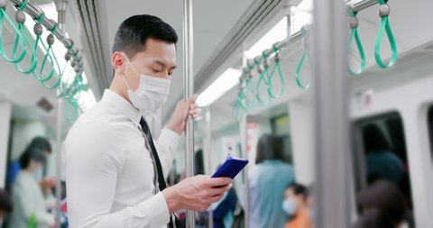Asian business man with surgical mask face protection use a smartphone and keep social distancing to crowd while commuting in the metro or train
