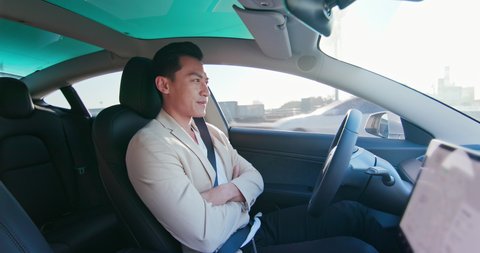 asian relaxed man experience to riding an autonomous self driving electric car and use autopilot function
