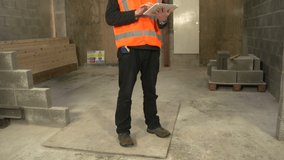 An Builder or Inspector or Engineer on Construction / Building Site.  He is looking through the plans on a Digital Tablet. Outdoors. Stock Video Clip Footage