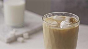 Close-up glass of refreshing cold coffee drink with milk, ice cubes and spoon stirring beverage on a light grey background. Slow motion, Full HD video, 240fps, 1080p.