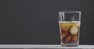 In a glass with ice and coffee pour milk with splashes around a dark background. Slow motion, 2K UHD video, 240fps, 1080p.