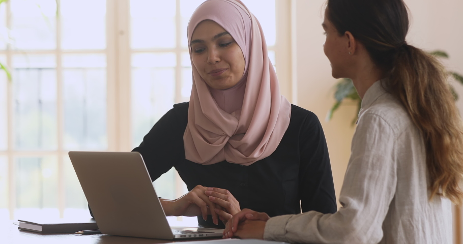 Smiling young asian muslim woman in hijab showing presentation on computer to female partner client, shaking hands making agreement, thanking for help, establishing partnership in modern office. Royalty-Free Stock Footage #1051730911