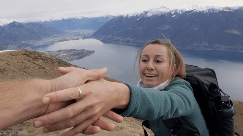 Hiker assisting teammate at mountain top giving a helping hand to reach summit. Point of view of male stretching out hand to female hiker helping her for the final steps to success 