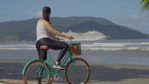 Santos / Brazil - April 2020  woman with face mask with her bike.Watch cruise ship sail away on the beach after corona virus lockdown
