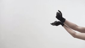 Wonderful female dancer in protective black latex gloves is performing a beautiful dance with her arms on a light background in a studio during COVID-19 quarantine. Video recording.