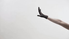 Elegant female dancer in a protective black latex glove is performing a beautiful dance with her arm on a light background in a studio during COVID-19 quarantine. Video recording.
