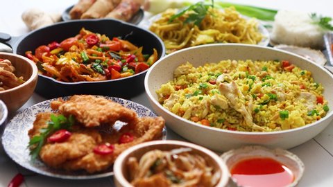 Family meal concept with asian food. Plates, pans and bowls full of tasty oriental dishes. People eating noodles chicken stir fry and vegetables. With ingredients, spices, sauces and chopsticks on