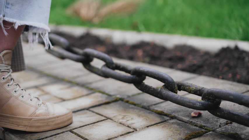 The girl puts her foot on a large chain and swings it with her foot. Close up. Walk around the city. Mood