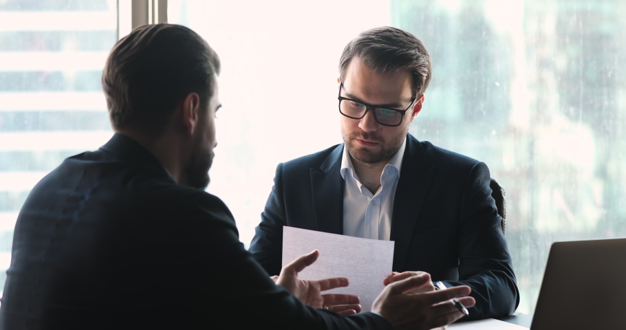 Concentrated businessmen discussing paper contract in office, shaking hands making agreement, establishing partnership at business meeting. Male client thanking financial advisor for consultation. Royalty-Free Stock Footage #1051750072